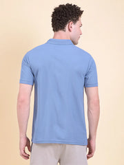 Man wearing a blue polo t-shirt  (DCYPHR Men's Element Polo - Denim Blue) against a beige background.