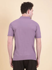 Man wearing a purple polo t-shirt (DCYPHR Men's Element Polo - Dusk Plum) against a beige background facing back camera.