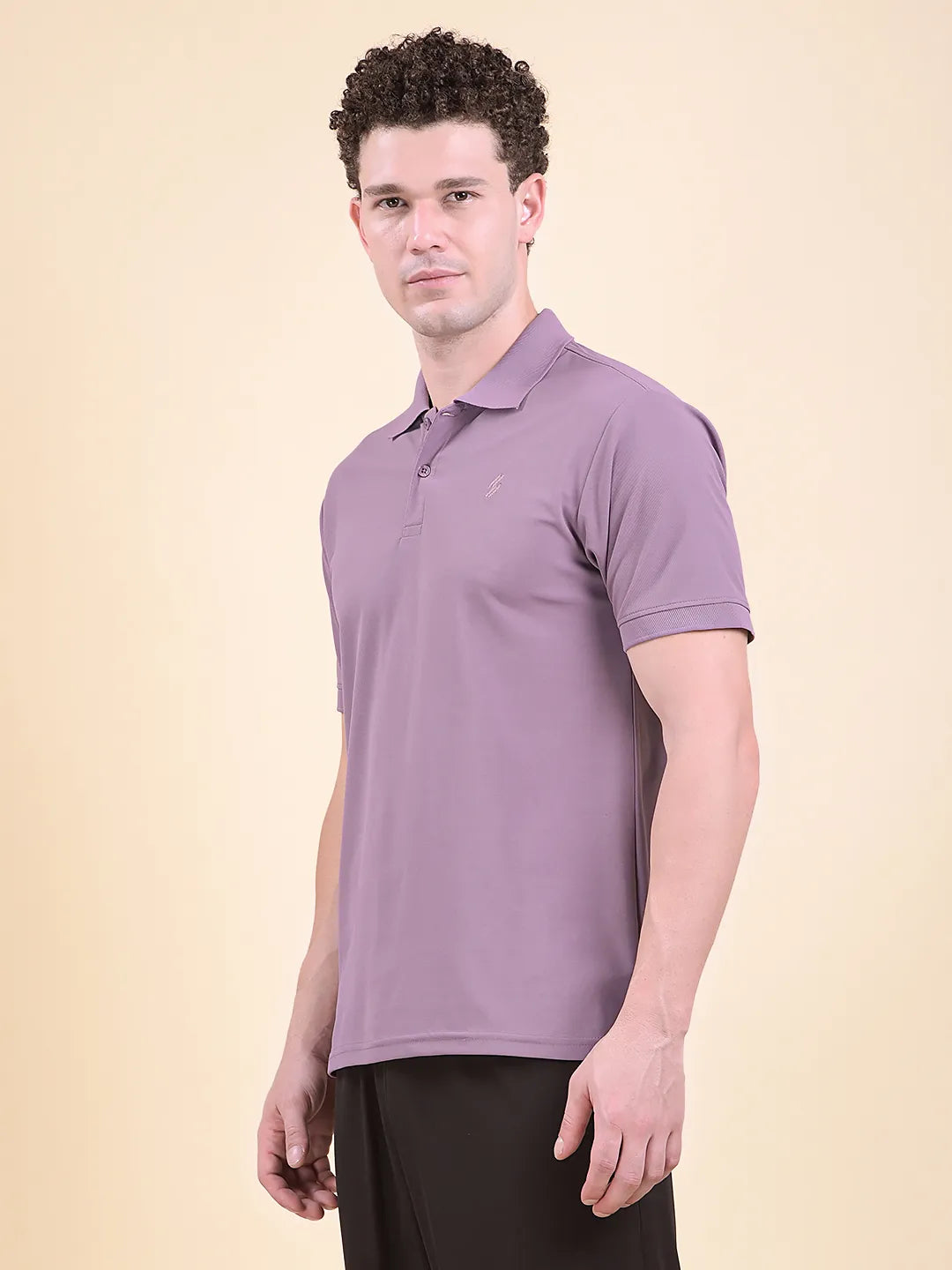 Man wearing a purple polo t-shirt (DCYPHR Men's Element Polo - Dusk Plum) against a beige background, facing sideways.