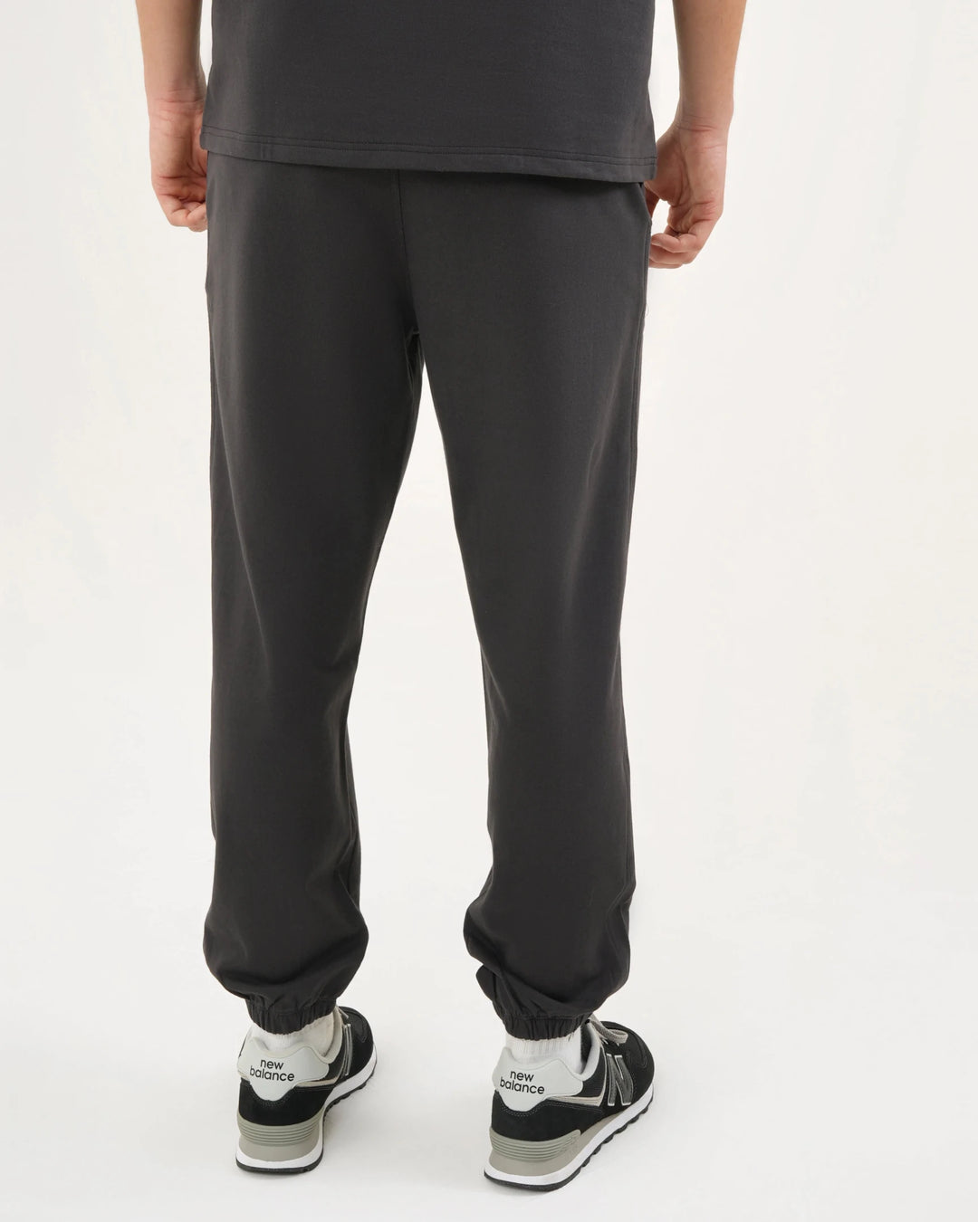 Person wearing black pants and black and white sneakers on a white background