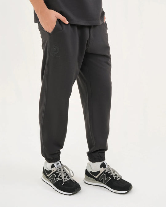 Person wearing black jogger pants and black sneakers on a white background