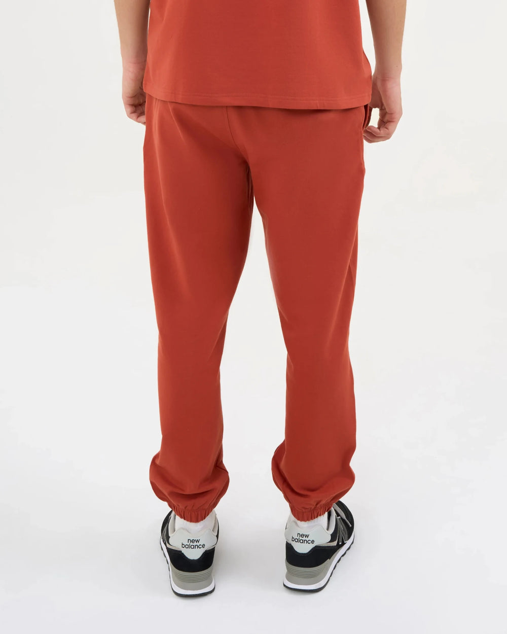 Person wearing DISCOVERY Men's Lounge Explorer Joggers - Burnt Orange and black sneakers.